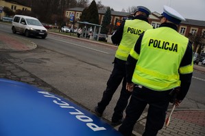 Na zdjęciu widać policjantów ruchu drogowego którzy stoją przy jezdni obserwując zachowanie uczestników ruchu drogowego