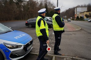 Zdjęcie przedstawia dwóch policjantów ruchu drogowego, którzy stoją przy radiowozie obserwując rejon przejścia dla pieszych