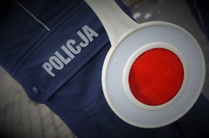 Na zdjęciu zbliżenie na tarczę STOP na tle granatowego munduru z napisem POLICJA