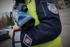 Na zdjęciu policjant ruchu drogowego trzyma urządzenie do pomiaru prędkości pojazdów