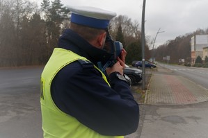 Zdjęcie - policjant ruchu drogowego stoi przy poboczu jezdni i urządzeniem mierzy prędkość pojazdów w rejonie przejścia dla pieszych