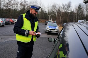 Zdjęcie: policjant ruchu drogowego przeprowadza kontrolę drogową. Z tyłu stoi radiowóz