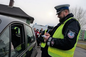 Zdjęcie: policjant ruchu drogowego przeprowadza kontrolę drogową stojąc przy samochodzie zatrzymanym do kontroli