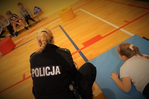 Zdjęcie: dzieci pod okiem policjantki pokonują tor przeszkód na sali gimnastycznej.