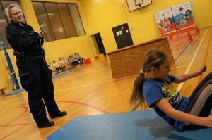 Zdjęcie: dzieci pod okiem policjantki pokonują tor przeszkód na sali gimnastycznej.