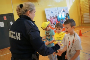 Zdjęcie: na sali gimnastycznej policjantka wręcza dzieciom nagrody