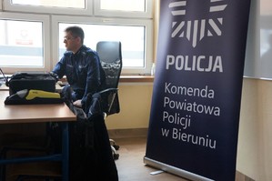 Na zdjęciu widzimy policjanta oraz baner z napisem Komenda Powiatowa Policji w Bieruniu