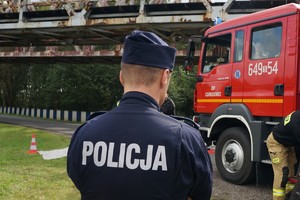 Na zdjęciu widzimy policjanta oraz wóz straży pożarnej