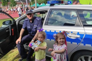 Na zdjęciu widzimy policjanta, radiowóz oraz dzieci w czasie festynu