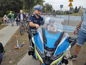 Na zdjęciu widzimy policjanta oraz motocykl służbowy, na którym siedzi dziecko