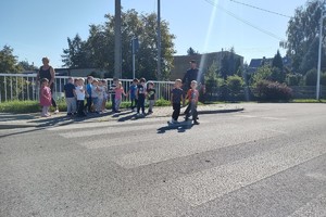 Na zdjęciu widzimy policjanta oraz sznupka wraz z grupą dzieci z przedszkola przechodzącą po przejściu dla pieszych