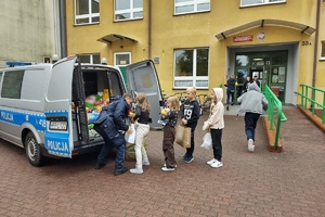 Na zdjęciu widzimy policjanta oraz uczniów pakujących dary do radiowozu