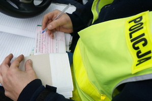 Na zdjęciu widzimy jak policjant wypisuje mandat karny