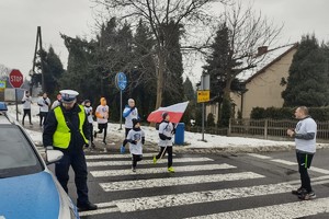 Na zdjęciu widzimy policjanta, radiowóz oraz osoby uczestniczące w biegu