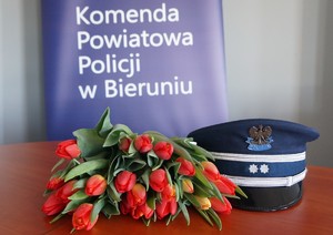 Na zdjęciu widzimy kwiaty, czapkę policyjną oraz napis Komenda Powiatowa Policji w Bieruniu