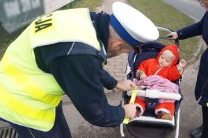 Na zdjęciu widzimy policjanta dającego element odblaskowy dziecku w wózku