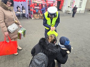 Na zdjęciu widzimy policjanta wręczającego elementy odblaskowe przechodniom