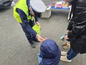 Na zdjęciu widzimy policjanta wręczającego elementy odblaskowe przechodniom