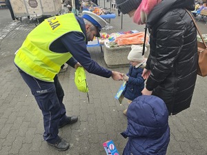 Na zdjęciu widzimy policjanta wręczającego elementy odblaskowe przechodniom