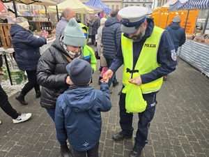 Na zdjęciu widzimy policjanta wręczającego elementy odblaskowe przechodniom