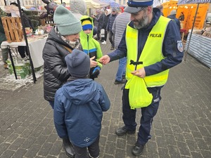 Na zdjęciu widzimy policjanta wręczającego elementy odblaskowe przechodniom