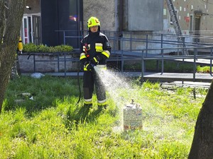 Na zdjęciu widzimy strażaka lejącego wodę na butlę z gazem